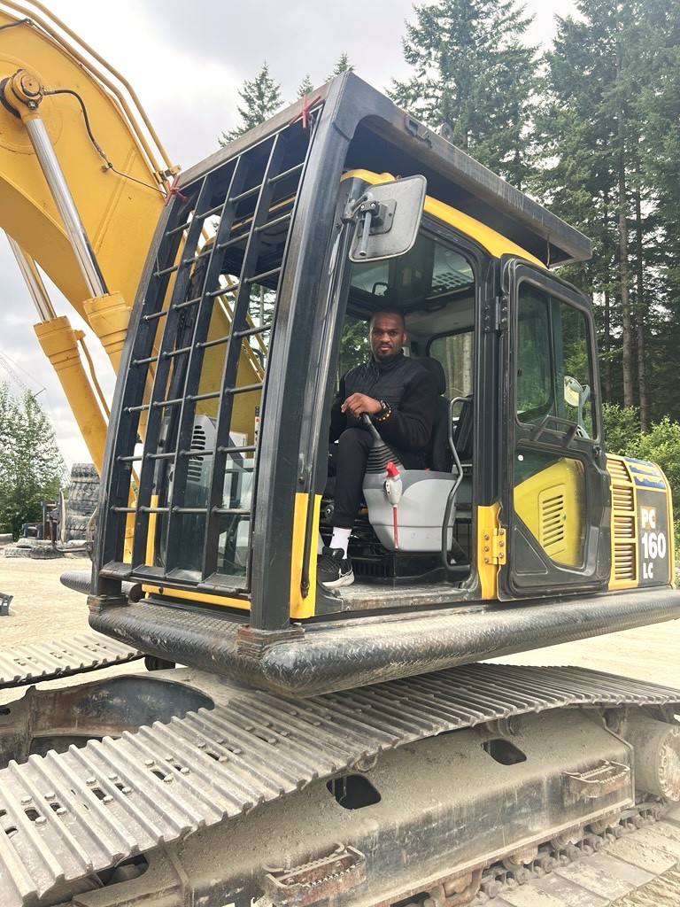 BCIB Comms Specialist, Will Balata, sits in an excavator.